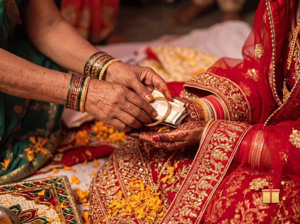 An older woman placing folded currency notes and a bangle into a young bride's hands